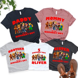 Op de afbeelding: Vijf T-shirts met korte mouwen met verjaardagsafbeeldingen. De shirts zijn marineblauw, mauve, grijs, wit en houtskool. Elk shirt heeft een andere tekst: "Daddy", "Mommy", "Brother", "5 Birthday Boy Oliver" en "Sister".