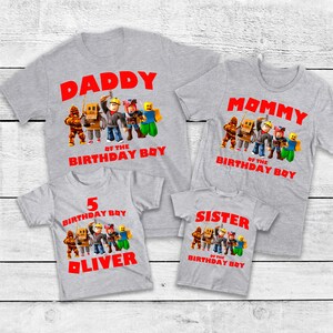 Op de afbeelding: Vier grijze t-shirts met rode tekst en cartoonkarakterafbeeldingen. De shirts lezen "DADDY", "MOMMY", "5 BIRTHDAY BOY OLIVER" en "SISTER". Elk shirt heeft een ander ontwerp.