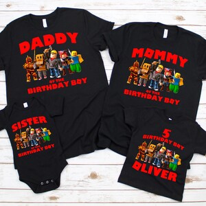 Op de afbeelding: Zwarte t-shirts met rode tekst en cartoonfiguren. De shirts lezen "Daddy of the Birthday Boy", "Mommy of the Birthday Boy", "Sister of the Birthday Boy" en "5 Birthday Boy Oliver".