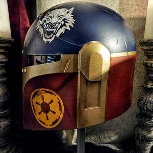 May include: A custom-painted helmet with a navy blue top and burgundy lower section. A white wolf graphic is on the top, and a yellow emblem is on the side. Gold-colored accents and details are present throughout the helmet.