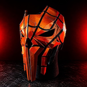K&ouml;nnte beinhalten: Eine orange-schwarze geometrische Maske mit einem bedrohlichen Design. Die Maske hat scharfe Winkel und Linien, mit einem dunklen Innenraum und einer strukturierten Oberfl&auml;che. Geeignet f&uuml;r Cosplay oder Kost&uuml;me.