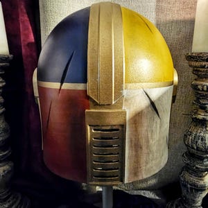 May include: A custom-painted helmet with a segmented design. The top is split between blue and yellow, with a gold central ridge. The lower sections are red and off-white, with gold accents and a vent detail. A unique cosplay item.