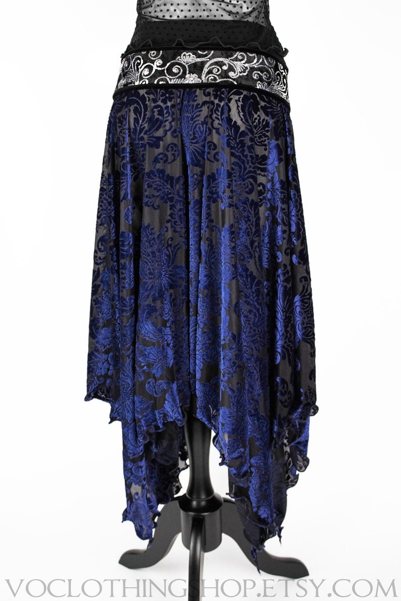 Pode incluir: Uma saia de veludo azul e preto com um padr&atilde;o floral. A saia &eacute; assim&eacute;trica, com uma frente mais longa e uma parte de tr&aacute;s mais curta. A saia tem uma bainha com babados.