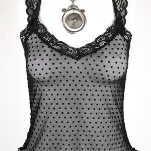 May include: Black polka dot mesh top with a lace trim and a silver pendant necklace.