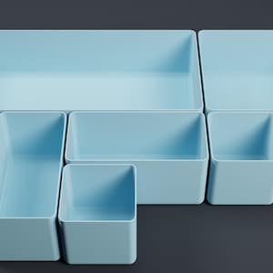 Può includere: Un set di sei contenitori portaoggetti azzurri di varie dimensioni. I contenitori sono rettangolari e quadrati, con finitura opaca. La disposizione suggerisce soluzioni di organizzazione e stoccaggio. I contenitori sono vuoti.