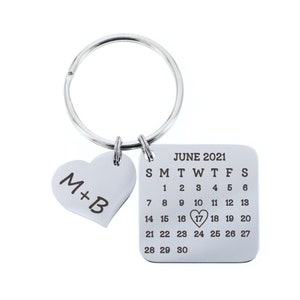 May include: Silver keychain with a heart charm engraved with "M+B" and a square charm with a calendar for June 2021, with the 17th circled.