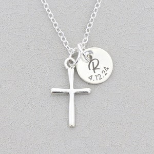 May include: Silver necklace with a cross pendant and a small round charm with the letter "R" and the date "4.12.24" engraved on it.