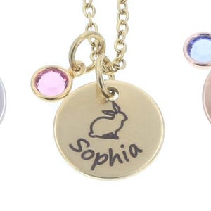 Three necklaces on white background. Each necklace has a small metal disc with a bunny outline engraved in the middle, a name around the edge, and colored crystal to the left. Each necklace is gold, rose gold, or silver.