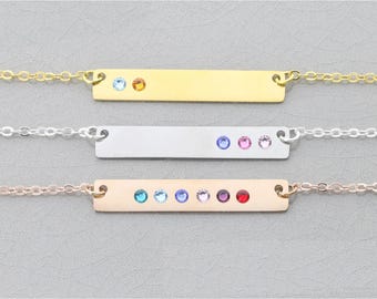 May include: Three bar necklaces in gold, silver, and rose gold. Each necklace features a rectangular bar with colourful gemstones. The gold necklace has two gemstones, the silver has three, and the rose gold has five.