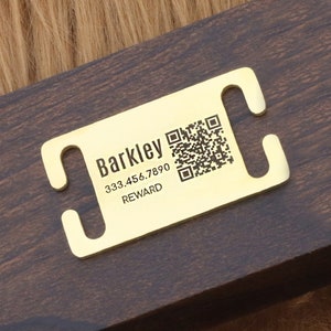 Op de afbeelding: Een goudkleurige huisdierpenning met afgeronde randen en een rechthoekige vorm. De penning heeft de naam "Barkley", een telefoonnummer en het woord "REWARD" erop gedrukt. Er is ook een QR-code aanwezig. De penning is ontworpen om aan een halsband te bevestigen.