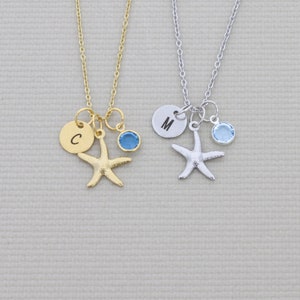 May include: Two necklaces with starfish pendants. One is gold-toned with a blue gem and a disc with the letter "C". The other is silver-toned with a blue gem and a disc with the letter "M". Both necklaces have delicate chains.