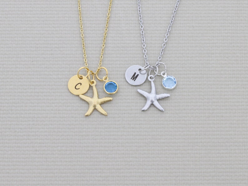 May include: Two necklaces with starfish pendants. One is gold-toned with a blue gem and a disc with the letter "C". The other is silver-toned with a blue gem and a disc with the letter "M". Both necklaces have delicate chains.