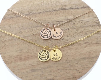 Può includere: Due collane da pallavolo dorate con ciondoli personalizzati. La collana superiore ha una catena in oro rosa e il ciondolo dice "4 Madison". La collana inferiore ha una catena in oro e il ciondolo dice "12 Eylar".
