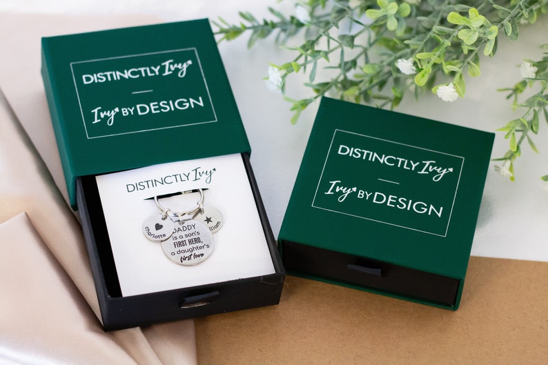DistinctlyIvy green drawer gift box and silver personalized keyring inside laying on white fabric with green leaves and white flowers in the background