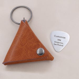 May include: A brown leather triangular keychain pouch with a silver metal snap and key ring. Beside it is a silver guitar pick with the text "Customize Me" and "Emojis too, See Photos!"