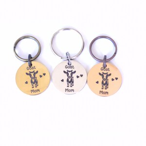 May include: Three round keychains with a goat illustration and the words "Goat Mom". The keychains are in gold, silver, and copper colors. Each keychain has a metal ring attached for keys.