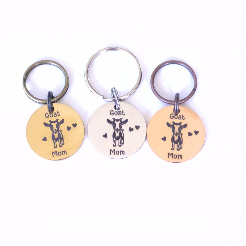 May include: Three round keychains with a goat illustration and the words "Goat Mom". The keychains are in gold, silver, and copper colors. Each keychain has a metal ring attached for keys.