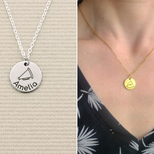 May include: Silver necklace with a round pendant featuring a megaphone and the name Amelia engraved on it.