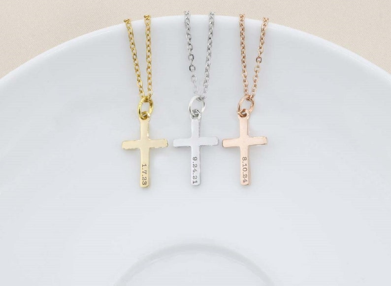 May include: Three gold, silver, and rose gold necklaces with cross pendants. Each cross has a different date engraved on it: 1.7.28, 8.24.21, and 8.10.84.