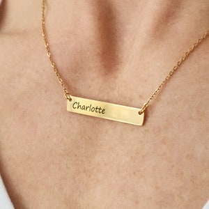May include: A gold chain necklace with a horizontal bar pendant engraved with the name "Charlotte".