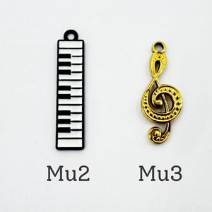 K&ouml;nnte beinhalten: Eine Sammlung von Musik-Anh&auml;ngern, darunter eine goldene Gitarre, ein schwarz-wei&szlig;er Klaviertasten-Anh&auml;nger, ein goldener Violinschl&uuml;ssel und ein kleinerer goldener Violinschl&uuml;ssel. Die Anh&auml;nger sind mit Mu1, Mu2, Mu3 und Mu4 beschriftet.