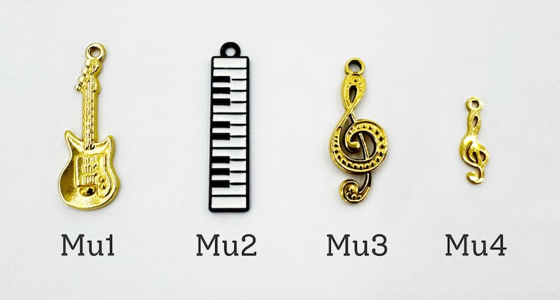 K&ouml;nnte beinhalten: Eine Sammlung von Musik-Anh&auml;ngern, darunter eine goldene Gitarre, ein schwarz-wei&szlig;er Klaviertasten-Anh&auml;nger, ein goldener Violinschl&uuml;ssel und ein kleinerer goldener Violinschl&uuml;ssel. Die Anh&auml;nger sind mit Mu1, Mu2, Mu3 und Mu4 beschriftet.