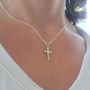 May include: A silver chain necklace with a silver cross pendant. The cross has the numbers "83431" engraved on it.