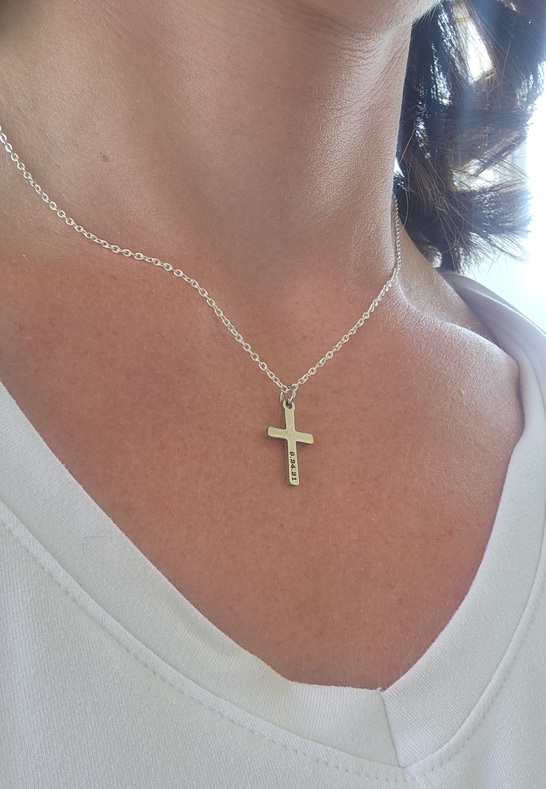 May include: A silver chain necklace with a silver cross pendant. The cross has the numbers "83431" engraved on it.