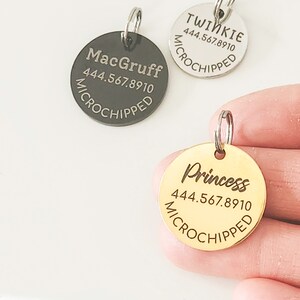May include: Three round silver and gold pet ID tags with engraved names and phone numbers. The tags read "MacGruff 444.567.8910 Microchipped", "Twinkie 444.567.8910 Microchipped", and "Princess 444.567.8910 Microchipped".