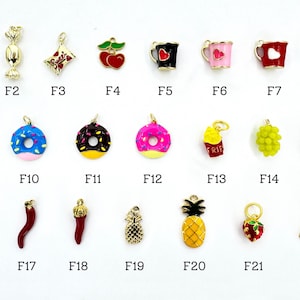 K&ouml;nnte beinhalten: Eine Sammlung goldfarbener Charms in verschiedenen Formen, darunter ein Apfel, S&uuml;&szlig;igkeiten, Kirschen, Donuts und eine Ananas. Jeder Charm hat eine Schlaufe zur Befestigung an Schmuck. Die Charms sind mit F1 bis F22 nummeriert.