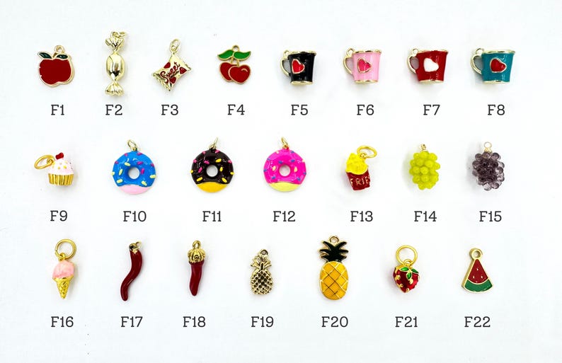K&ouml;nnte beinhalten: Eine Sammlung goldfarbener Charms in verschiedenen Formen, darunter ein Apfel, S&uuml;&szlig;igkeiten, Kirschen, Donuts und eine Ananas. Jeder Charm hat eine Schlaufe zur Befestigung an Schmuck. Die Charms sind mit F1 bis F22 nummeriert.