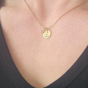 Model in black vneck shirt is wearing a gold necklace with pink crystal and small god disc engraved with bunny outline in the middle and name around the edge.