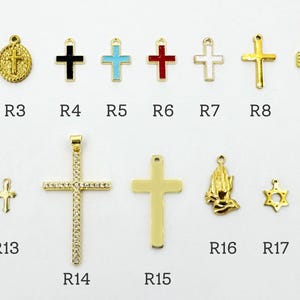 K&ouml;nnte beinhalten: Eine Sammlung goldfarbener religi&ouml;ser Anh&auml;nger und Anh&auml;nger, darunter Kreuze, Engel und ein Davidstern. Verschiedene Designs weisen farbige Emaille- und Kristallakzente auf. Die Anh&auml;nger sind auf einer wei&szlig;en Oberfl&auml;che angeordnet.