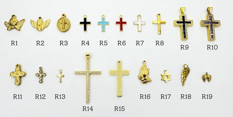 K&ouml;nnte beinhalten: Eine Sammlung goldfarbener religi&ouml;ser Anh&auml;nger und Anh&auml;nger, darunter Kreuze, Engel und ein Davidstern. Verschiedene Designs weisen farbige Emaille- und Kristallakzente auf. Die Anh&auml;nger sind auf einer wei&szlig;en Oberfl&auml;che angeordnet.