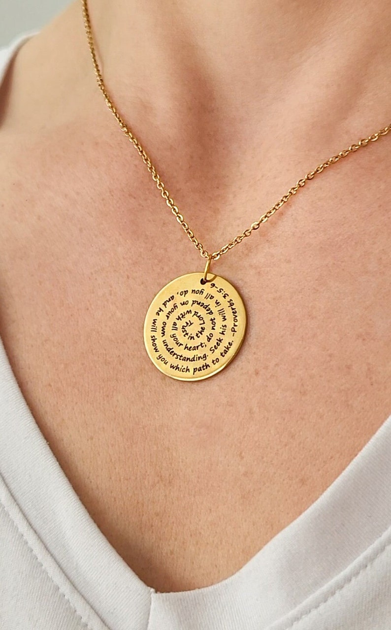 May include: Gold necklace with a round pendant featuring an inspirational quote in a spiral design. The quote reads: "Lord, do not depend on your own understanding; in all you do, and he will show you which path to take. -Proverbs 3:5-6"