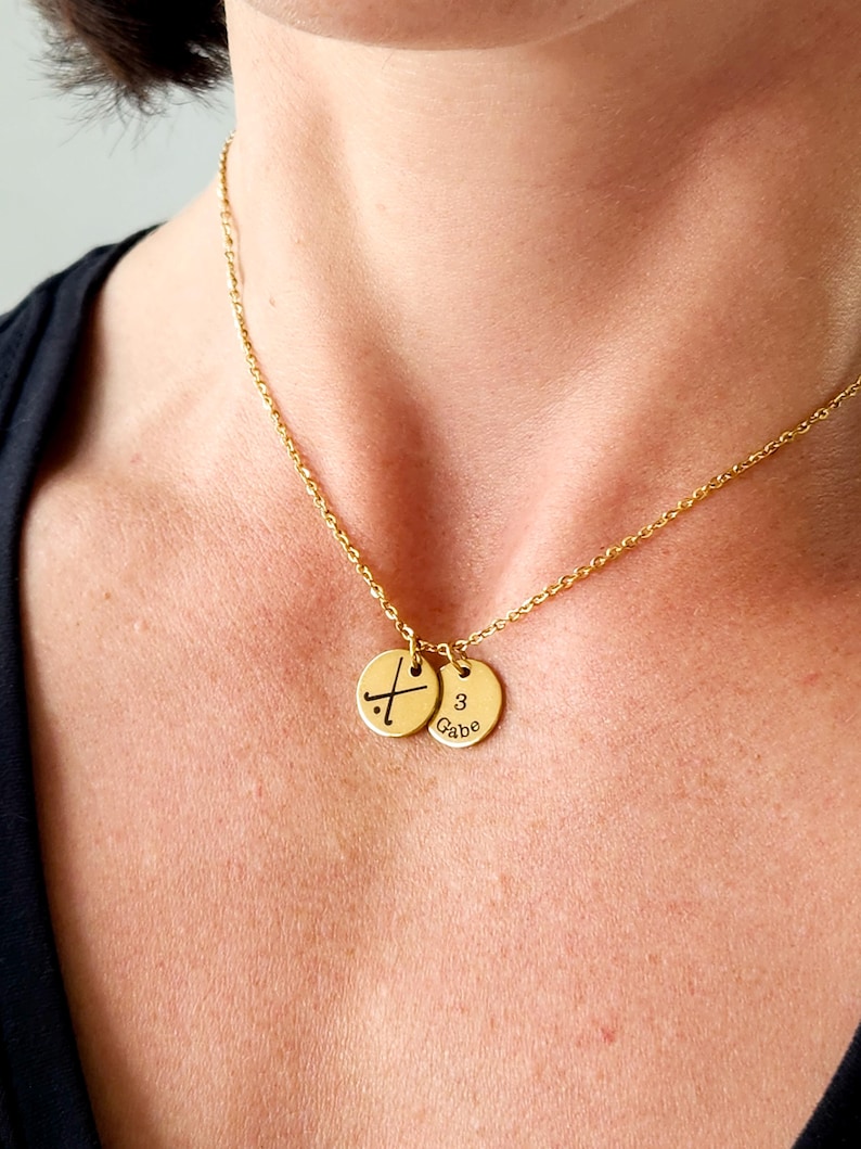 model's neck with black shirt on, wearing gold necklace with two discs showing field hockey symbol and number and name of player
