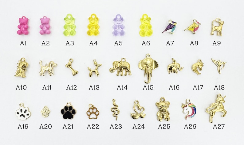 K&ouml;nnte beinhalten: Eine Sammlung kleiner Charms in verschiedenen Formen und Farben. Die Charms umfassen Gummib&auml;rchen, V&ouml;gel, Tiere und Pfotenabdr&uuml;cke. Jeder Charm ist mit einer Buchstaben- und Zahlenkombination beschriftet.