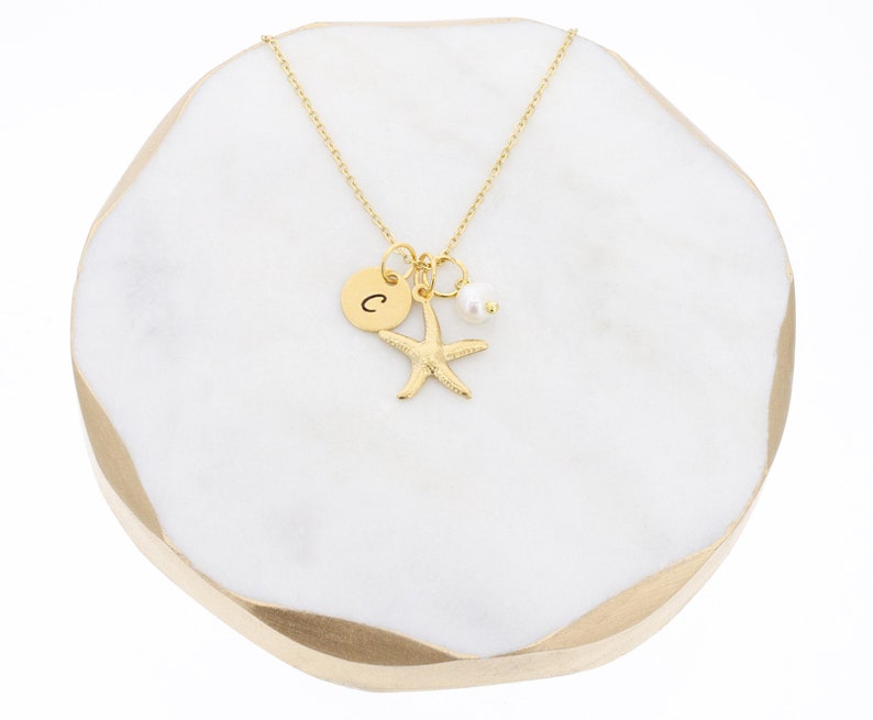 May include: Gold necklace with a charm of a starfish, a pearl, and a small disc with the letter "C" engraved on it.