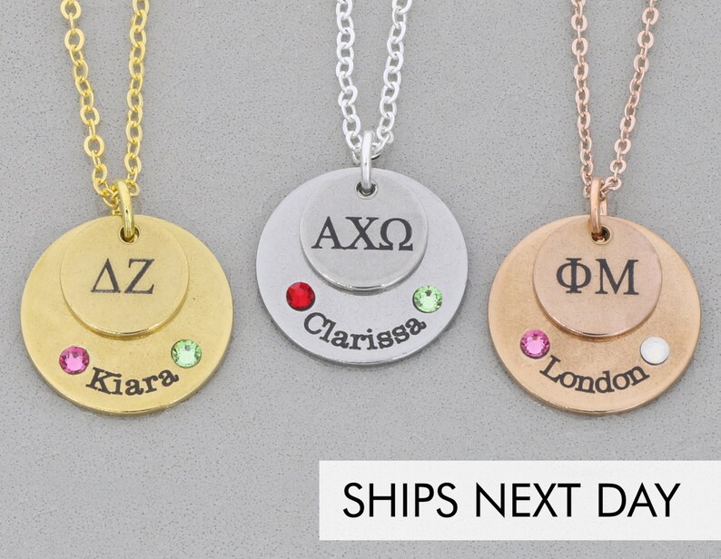 3 necklaces Gold Silver rose-gold. Each necklace has a dime sized disc stacked on a quarter sized disc. The small discs have 2-3 Greek letters engraved. The larger discs have names engraved along the bottom and birthstones glued on either side