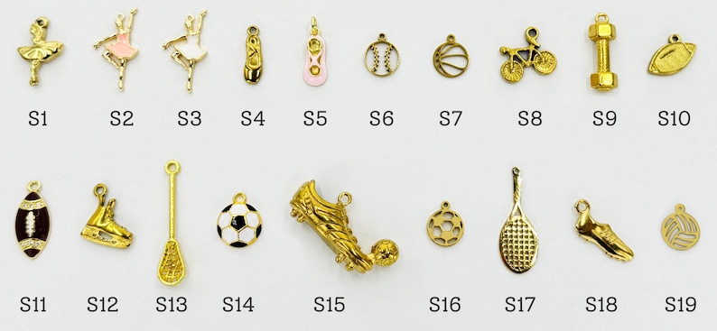 K&ouml;nnte beinhalten: Eine Sammlung goldfarbener Charms in verschiedenen Formen, darunter Ballettt&auml;nzerinnen, Sportger&auml;te wie ein Football, ein Fu&szlig;ball und ein Tennisschl&auml;ger sowie andere Artikel. Jeder Charm ist mit einem Buchstaben und einer Nummer gekennzeichnet.