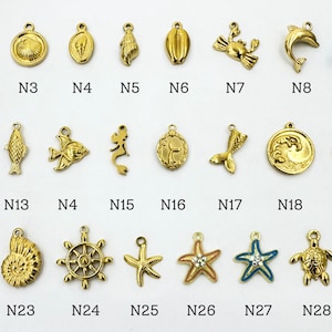 K&ouml;nnte beinhalten: Eine Sammlung goldfarbener nautischer Charms, darunter Anker, Muscheln, Delfine, Seesterne und Seepferdchen. Jeder Charm hat eine Schlaufe zum Befestigen an Schmuck oder anderen Bastelarbeiten. Die Charms sind in Reihen und Spalten angeordnet, wobei jeder Charm mit einer Nummer versehen ist.