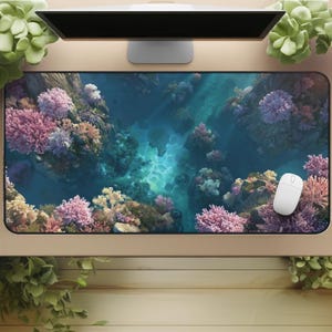 Peut inclure: Un grand tapis de souris rectangulaire représentant une scène sous-marine vibrante avec des récifs coralliens roses, jaunes et oranges. Le fond est bleu foncé, et une souris d'ordinateur blanche repose sur le tapis.