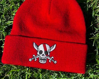 May include: Red knit beanie with a white skull and crossbones design. The skull has a red eye patch and horns.