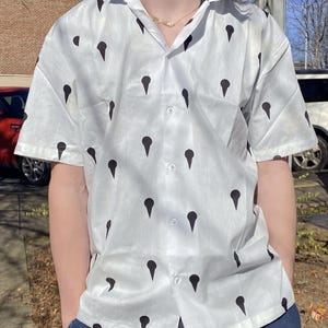 May include: A white short-sleeved button-down shirt with a black pattern of repeating teardrop shapes.