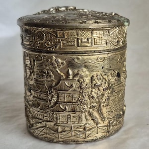 Vintage metal cylindrical trinket box adorned with intricate detailing featuring traditional Asian landscapes - 6.5cm tall