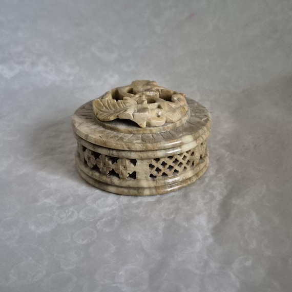 Round intricately carved soap stone trinket box with raised foliage decorative pattern to lid - 7.5cm diameter