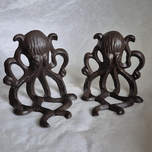 Puede incluir: Dos sujetalibros de pulpo de hierro fundido en un acabado marrón oscuro. Cada sujetalibros presenta un diseño de pulpo con tentáculos detallados y una superficie texturizada. Los sujetalibros están diseñados para sostenerse en posición vertical y sujetar libros.