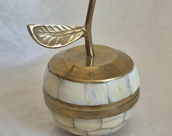 May include: A decorative apple-shaped container featuring a polished brass lid and stem with a textured leaf. The body is constructed from small, iridescent white shell tiles arranged in a grid pattern, separated by thin brass bands.