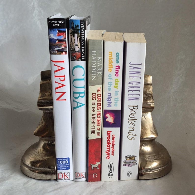 May include: A set of books held between two gold-colored chess piece bookends. The books include titles like "Japan," "Cuba," and "The Curious Incident of the Dog in the Night-Time."