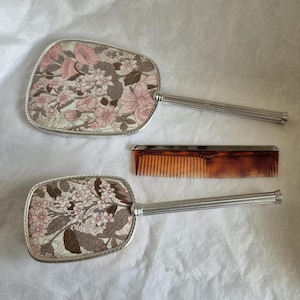 Vintage 3 piece vanity set, attractive decoration depicts floral design in pink, red and white; mirror, hairbrush and comb.